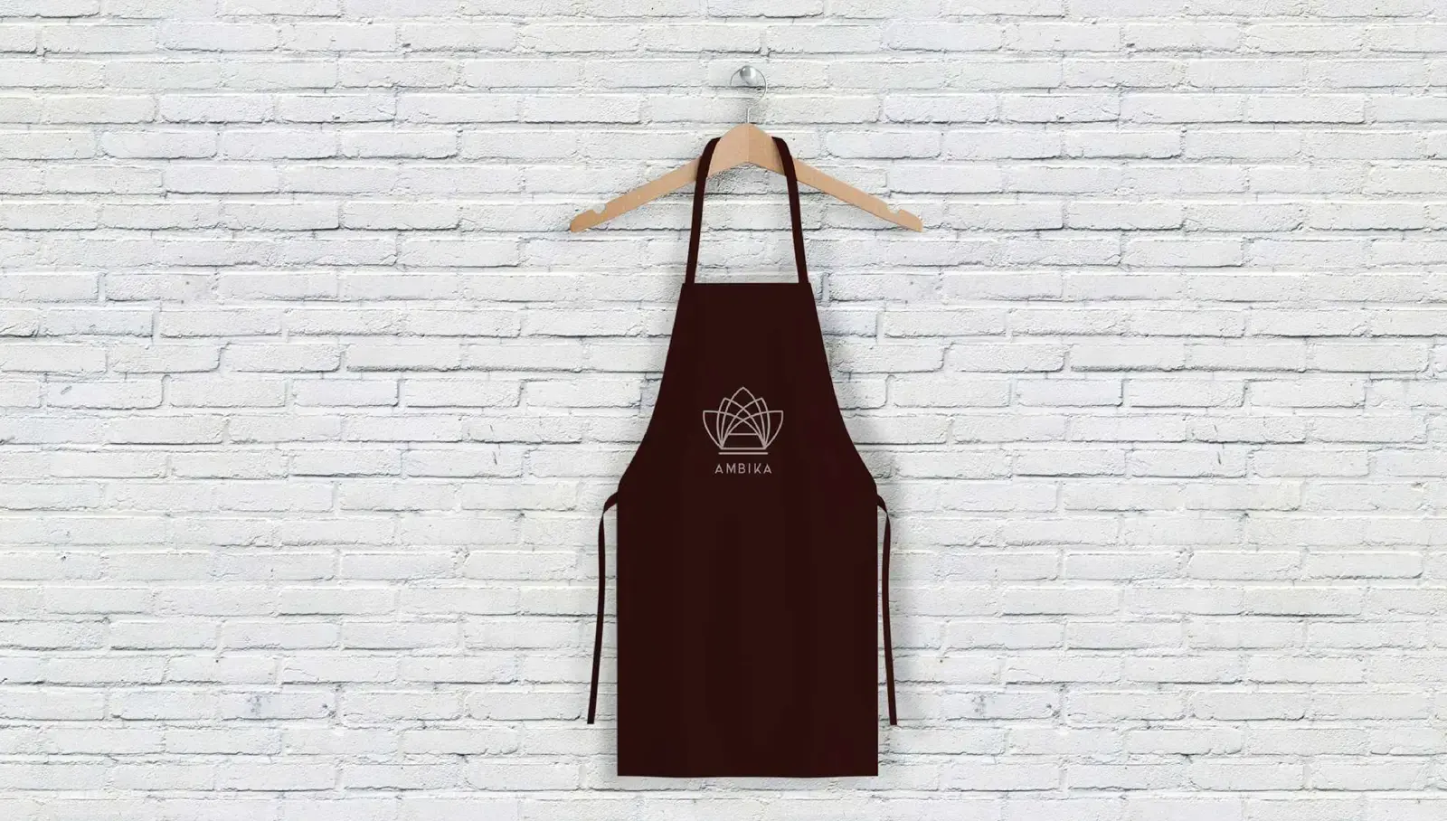 Deep oxblood Ambika service apron displayed against a white brick wall